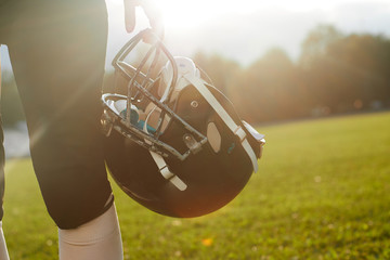 Girl American football player holding helmet on a background of dawn.