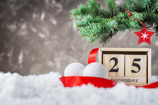 Wooden Calendar Set On The 25 Of December With Holiday Balls And Red Ribbon On Snow On Gray Background. Christmas Date On Calendar. 25 St Of December. Empty Copy Space For Inscription. Xmas Concept.