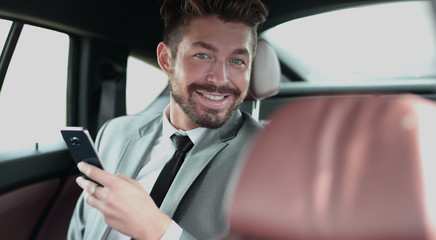 Happy young businessman using mobile phone in back seat of car