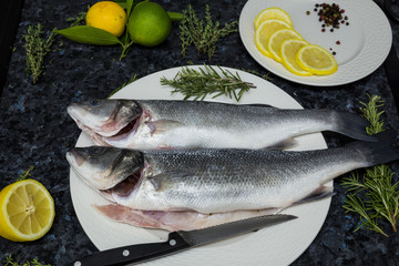 Raw fish with lemon and rosemary on a white plate.