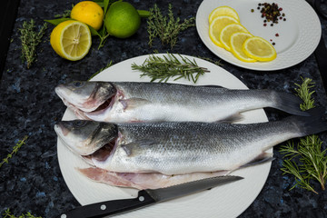 Raw seabass lies on a white plate with rosemary and lemon.