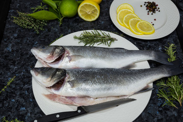 Raw fish with lemon and rosemary on a white plate.