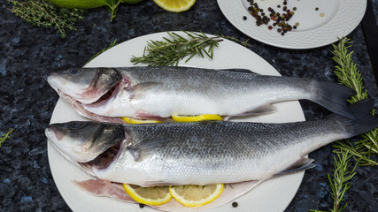 Raw fish with lemon and rosemary on a white plate.