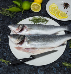 Raw fish with lemon and rosemary on a white plate.