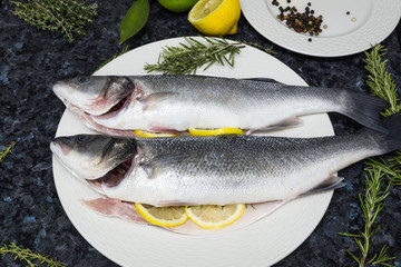 Raw fish with lemon and rosemary on a white plate.
