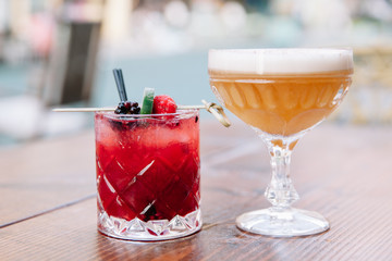 Two colorful alcoholic cocktails on a wooden table outdoors