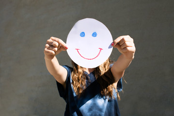 Teenage girl holding a drawing of a smiley in front of her face