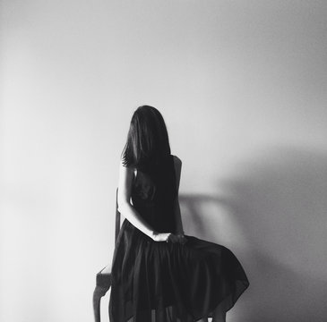 Woman wearing a long black dress sits with her face hidden behind her hair