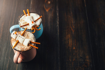 a mug with hot chocolate on a wooden table with a marshmallow man who is resting in a mug