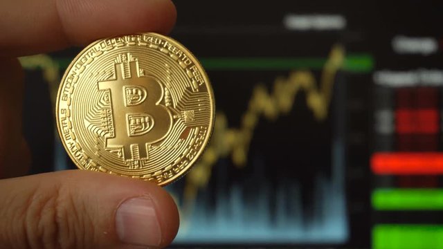 Bitcoin coin in hands of man opposite trading terminal