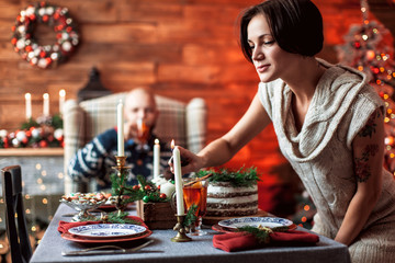 Beautiful young couple cover the table in preparation for Christmas dinner in the beautifully decorated New Year interior with Christmas tree