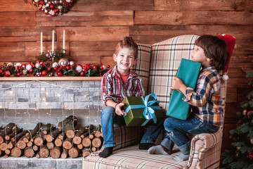 Beautiful happy laughing children brothers  play with gifts in hand in a Christmas interior with a Christmas tree. The concept of a family holiday