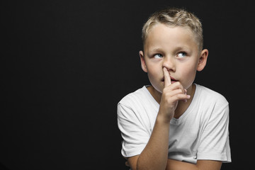little blond boy thinks and drills with the pointing finger in the nose