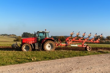 Fototapeta premium Red tractor pole field. Autumn field work. Life on the farm. Agricultural landscape in the Czech Republic.