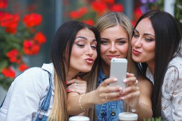 Group of girlfriends making a selfie photo at the mobile camera an smiling. Pretty women having fun at the cafe. Young girls laughing