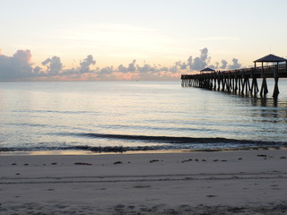 Obraz premium Watching the sunset and waves crashing on the beach next to a pier