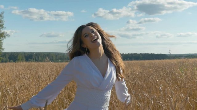 A singer in a white dress is singing on a field with wheat.