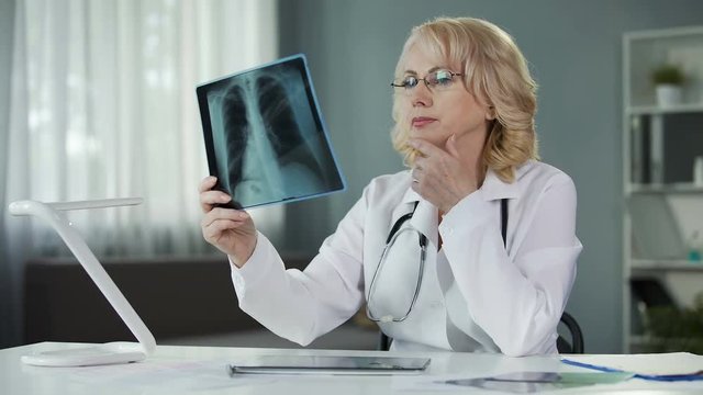 Doctor examining X-ray of patient's lungs making notes in medical records