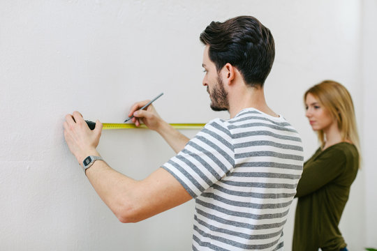 Young couple measuring the wall to hanging a picture.