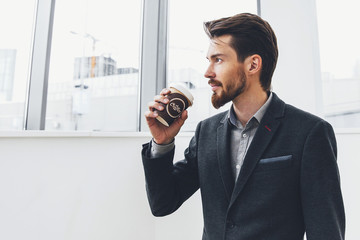 Young businessman standing with coffee in hand is against the window