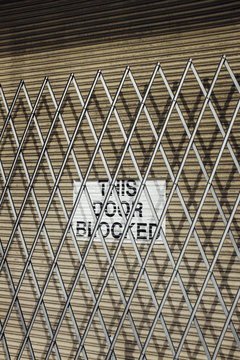 Metal fence across warehouse door with sign reading "THIS DOOR BLOCKED"