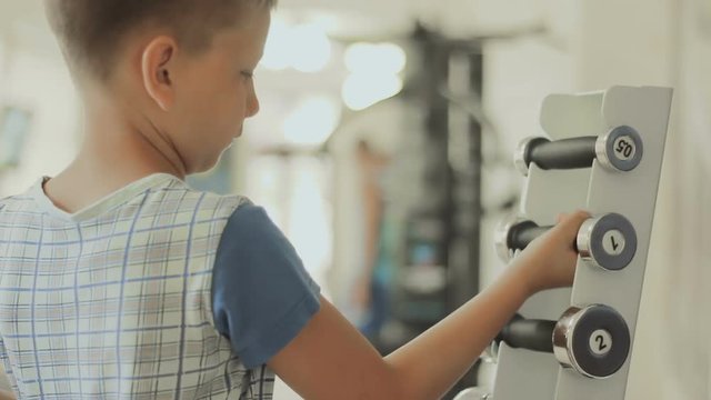 the boy chooses dumbbells for his training in the gym. The concept of sporting motivation to increase. Teenager cares about his body, figure, appearance and health from the childhood