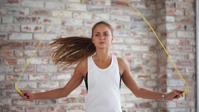 Sports woman is skipping rope indoor. Intense work-out of young pretty female athlete before training in gymnasium.
