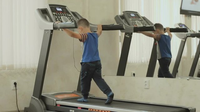 the kid walks on the treadmill. Baby is exercising in the gym near the mirror. Boy cares about his body, figure, appearance and health from the childhood. The concept of a healthy lifestyle