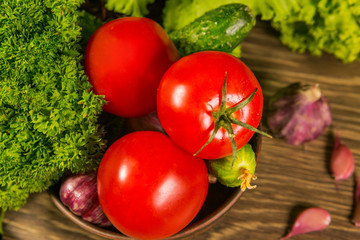 Fresh ripe tomatoes on a wooden table with a green salad on the background. Fresh vegetables. Delicious vegetarian food. Salad.
