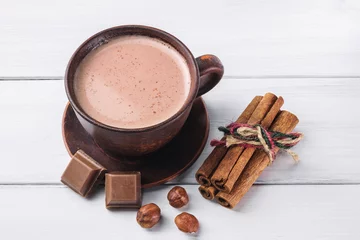 Papier Peint photo autocollant Chocolat Cacao chaud au lait dans une tasse d& 39 argile brune, cubes de chocolat cassés, bâtons de noisette et de cannelle sur des planches de bois blanches