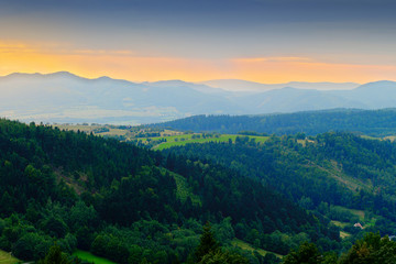 Fototapeta na wymiar Vast panorama view of foggy valley in the Owl Mountains with silhouette of Sudetes mountain range at dusk. Mountainous countryside landscape in south-west Poland.