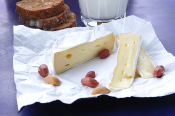 Camembert cheese, a glass of milk, pomegranate, peanut grains and bread on white cloth and a dark...