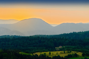 Fototapeta premium Vast panorama view of valley in the Owl Mountains with silhouette of Sudetes mountain range at dusk. Mountainous countryside landscape in south-west Poland.