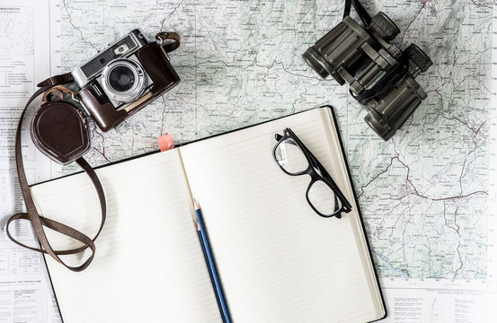 Overhead view of camera, eyeglasses, notebook on world map 