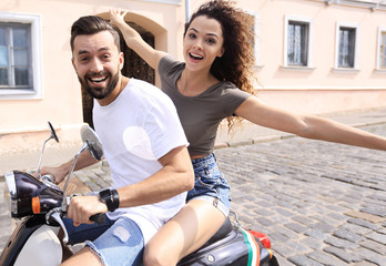 Cheerful young couple riding a scooter and having fun