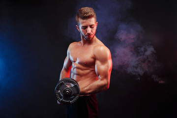 Strong athletic young man with huge muscles working out with dumbbell in hand