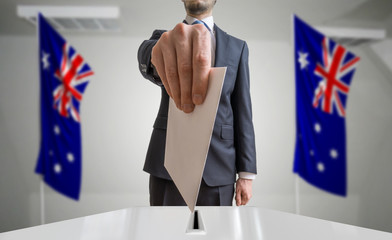 Election or referendum in Australia. Voter holds envelope in hand above ballot. Australian flags in...