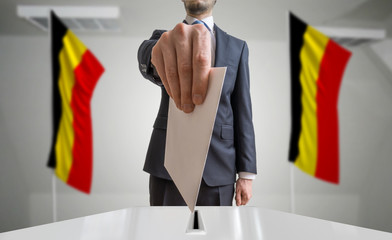 Election or referendum in Belgium. Voter holds envelope in hand above ballot. Belgian flags in...