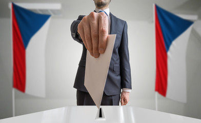 Election or referendum in Czech Republic. Voter holds envelope in hand above ballot. Czech flags in...