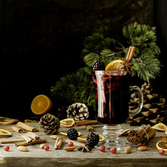glass of hot mulled wine for the new year with ingredients for cooking, nuts and Christmas decorations