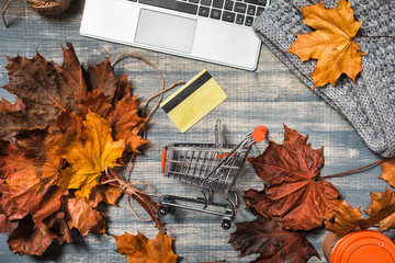 Shopping cart on wooden Desktop. Workspace with laptop, maple yellow and red leaves, credit card on...