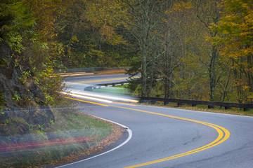 Twisting curvy road winding through fall colorful trees in national park with long exposure car streaks showing motion speed and transportation