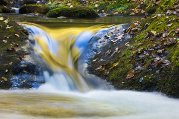 Beautiful colorful flowing water reflecting fall leaves and blue sky nature forest background