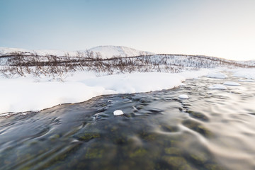 Water stream with rocks in a winter landscape in twilight.