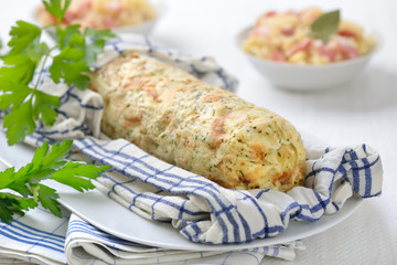 Deftiger bayerischer Serviettenknödel im Geschirrtuch gekocht und serviert, Sauerkraut mit Speck im Hintergrund – Bavarian bread dumpling cooked in a rolled up tea towel, sauerkraut the background