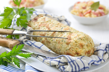 Deftiger bayerischer Serviettenknödel im Geschirrtuch gekocht und serviert, Sauerkraut mit Speck im Hintergrund – Bavarian bread dumpling cooked in a rolled up tea towel, sauerkraut the background