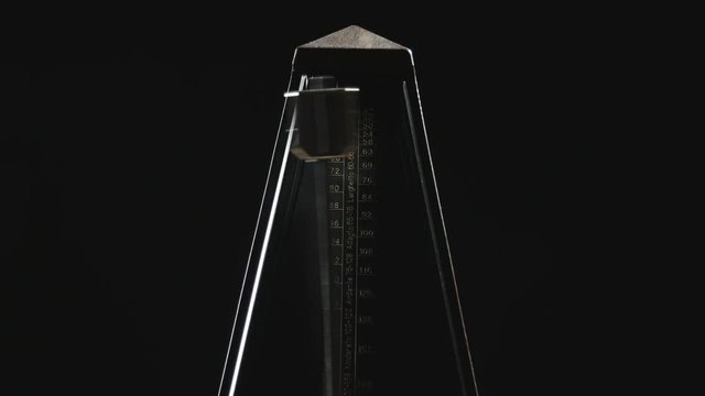 Close-up shot of vintage metronome with golden pendulum beats slow rhythm on the dark background