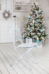 Stylish Christmas interior with an elegant blue decorations. Comfort home. White iron chair. Christmas tree with presents underneath in living room