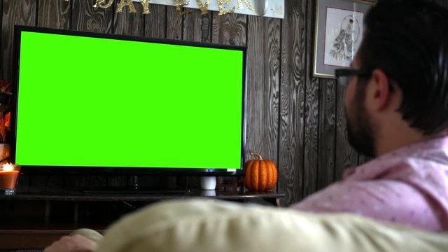 Millennial Male Talks To His Smart Voice Remote While Watching Generic Green Screen Tv