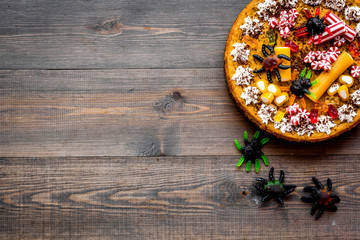 Gummy spiders crawls toward pie for halloween on wooden background top view copyspace